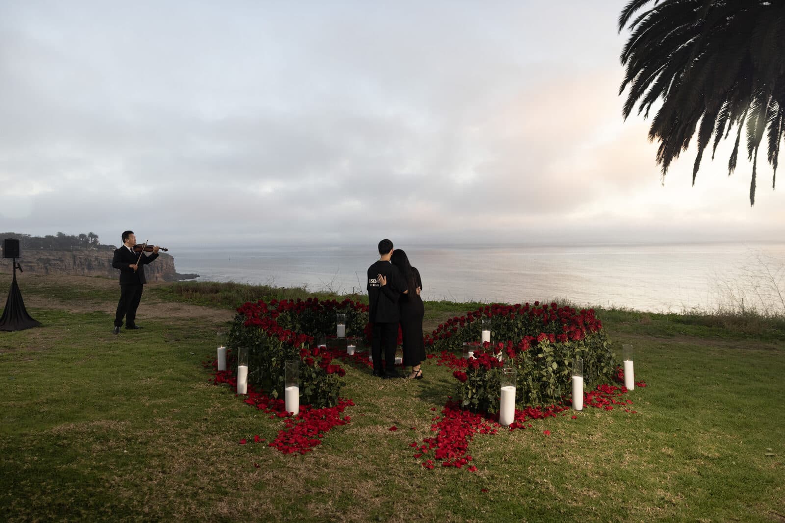 Oceanfront proposal at golden hour with a live violinist and a rose-petal heart
