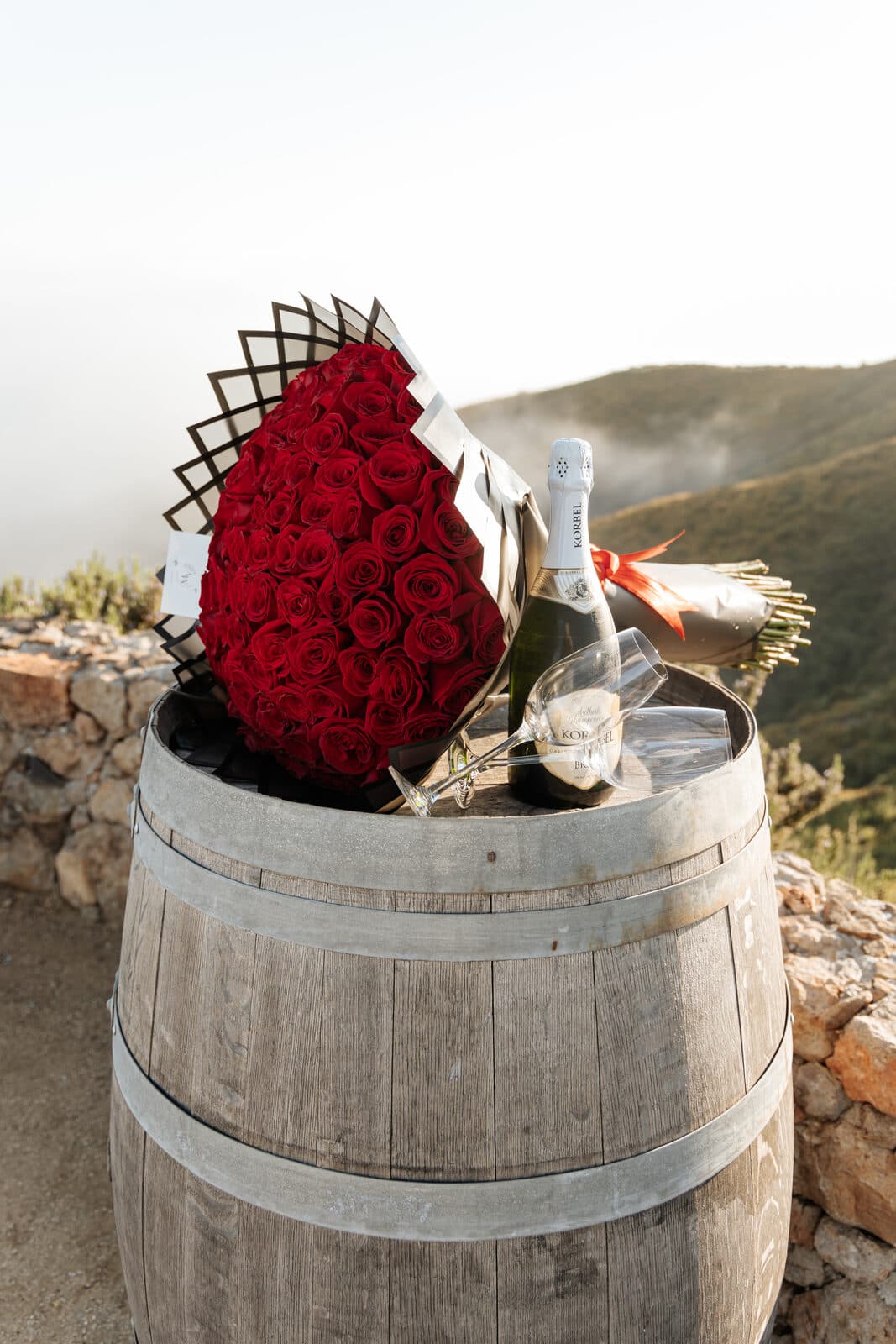 Red roses and champagne set up on a wine barrel at a hilltop proposal