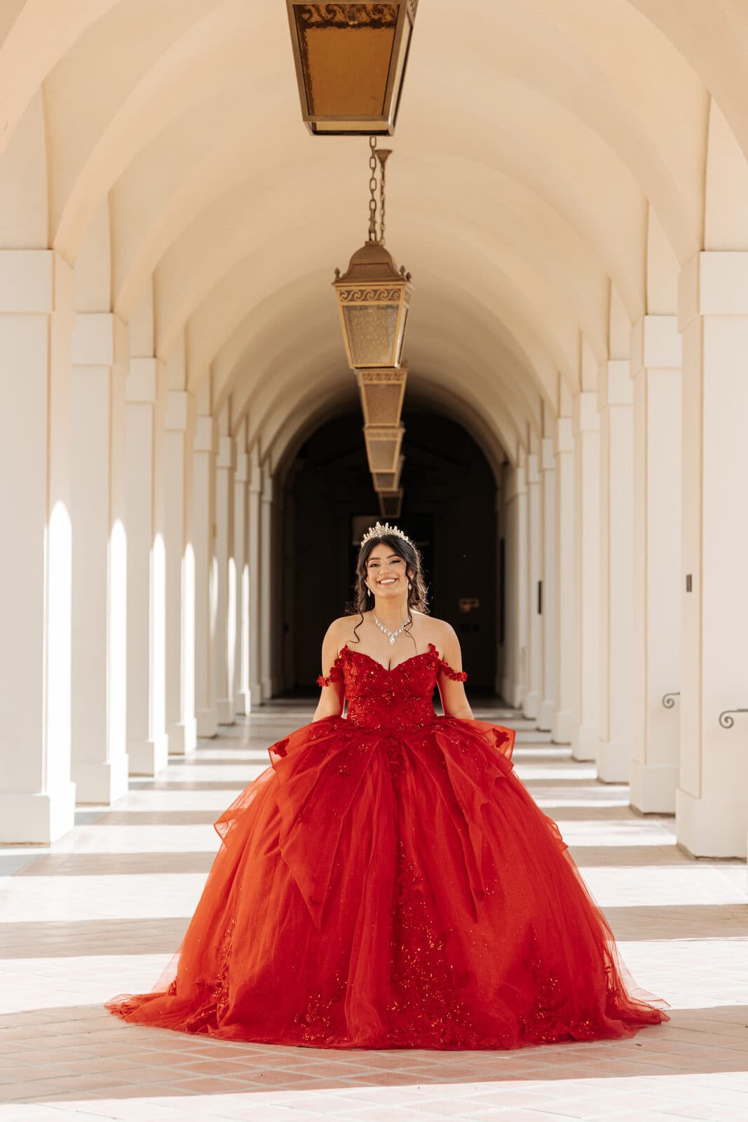 Quinceañera in a flowing red gown beneath a historic Pasadena archway, photographed by SoCal Shooter